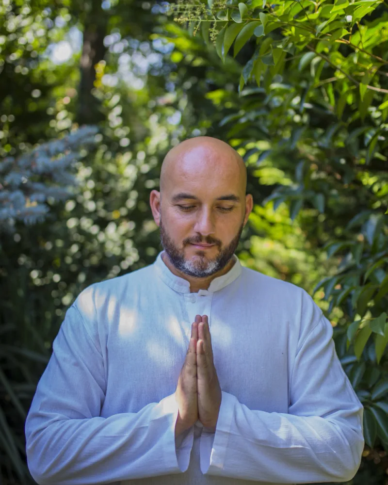 Doğada beyaz kıyafetle namaste pozisyonunda duran yoga eğitmeni