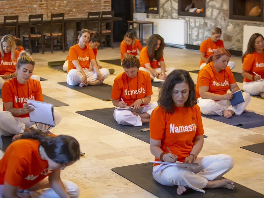 Taş salonda not tutan turuncu tişörtlü yoga eğitmenliği öğrencileri