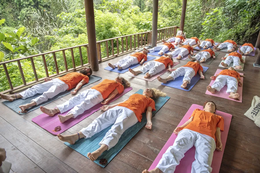 Ahşap terasta matlarında sırt üstü gevşeme (savasana) yapan beyaz kıyafetli katılımcılar